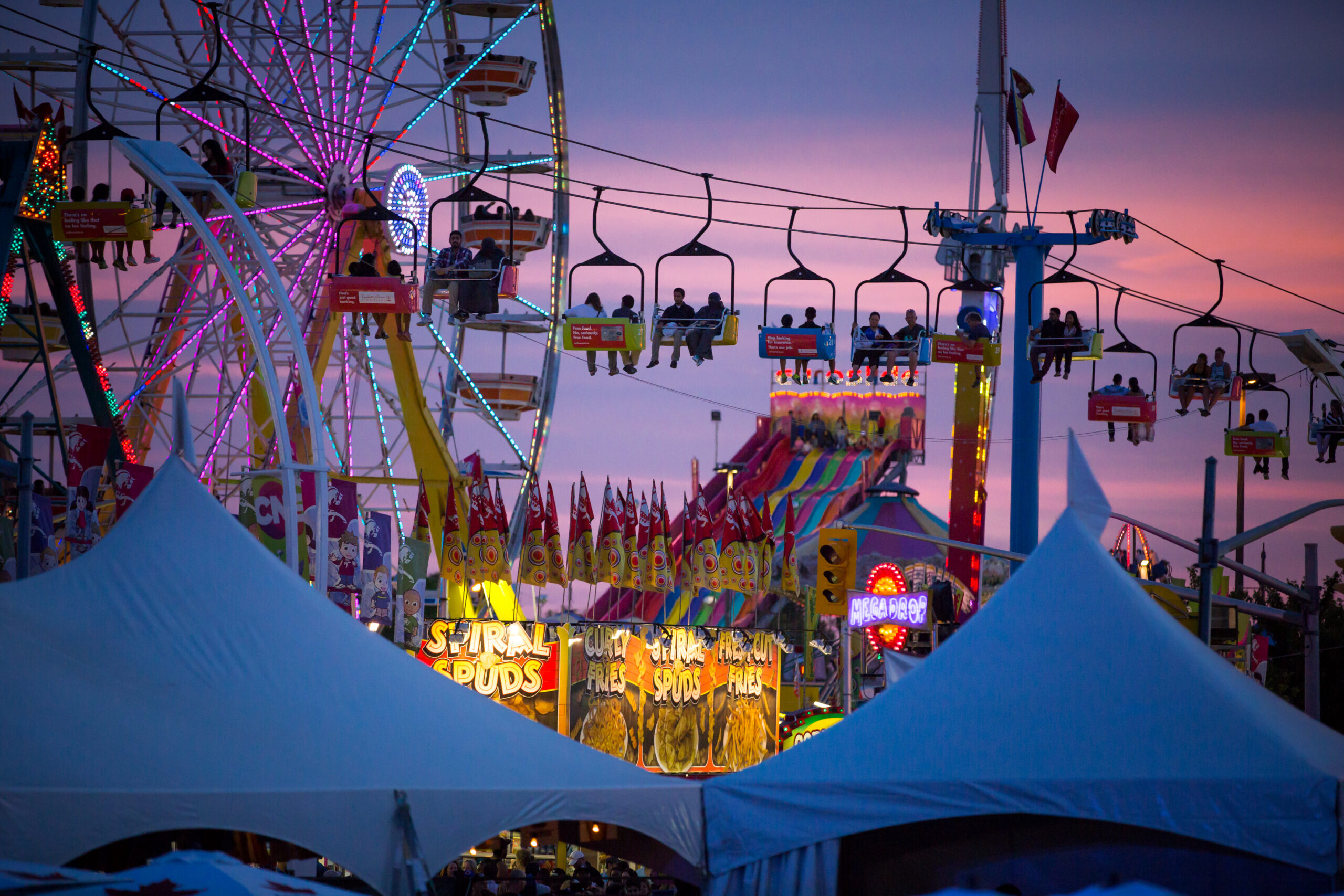 Aerial view of the Sky Ride and a Ferris Wheel in the CNE Midway at dusk.