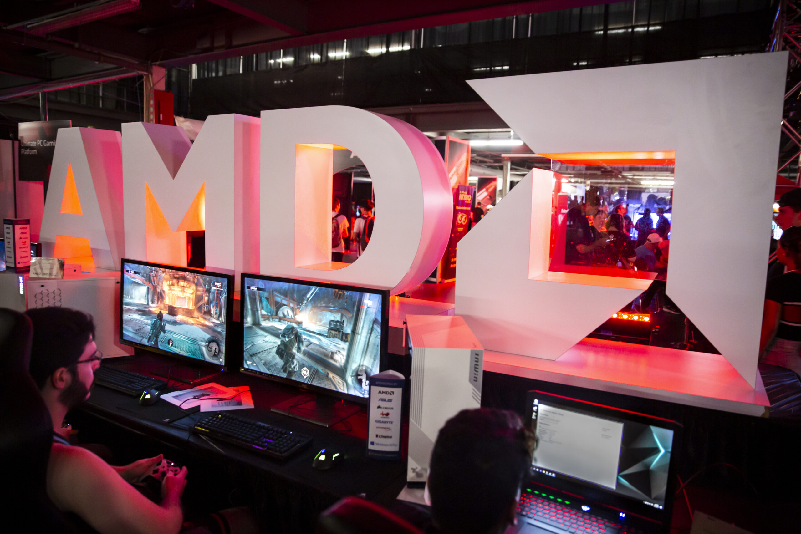 A man infront of two computer screens with AMD logo in the background in large letters