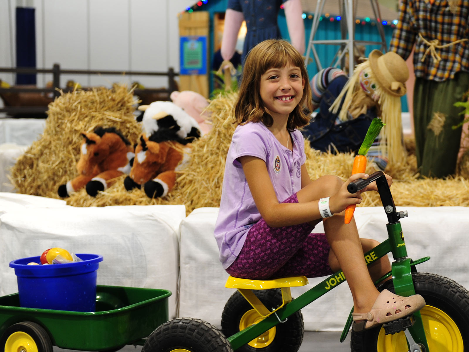 Image of a girl sitting on a John Deer tricycle in part of the Farm exhibit.