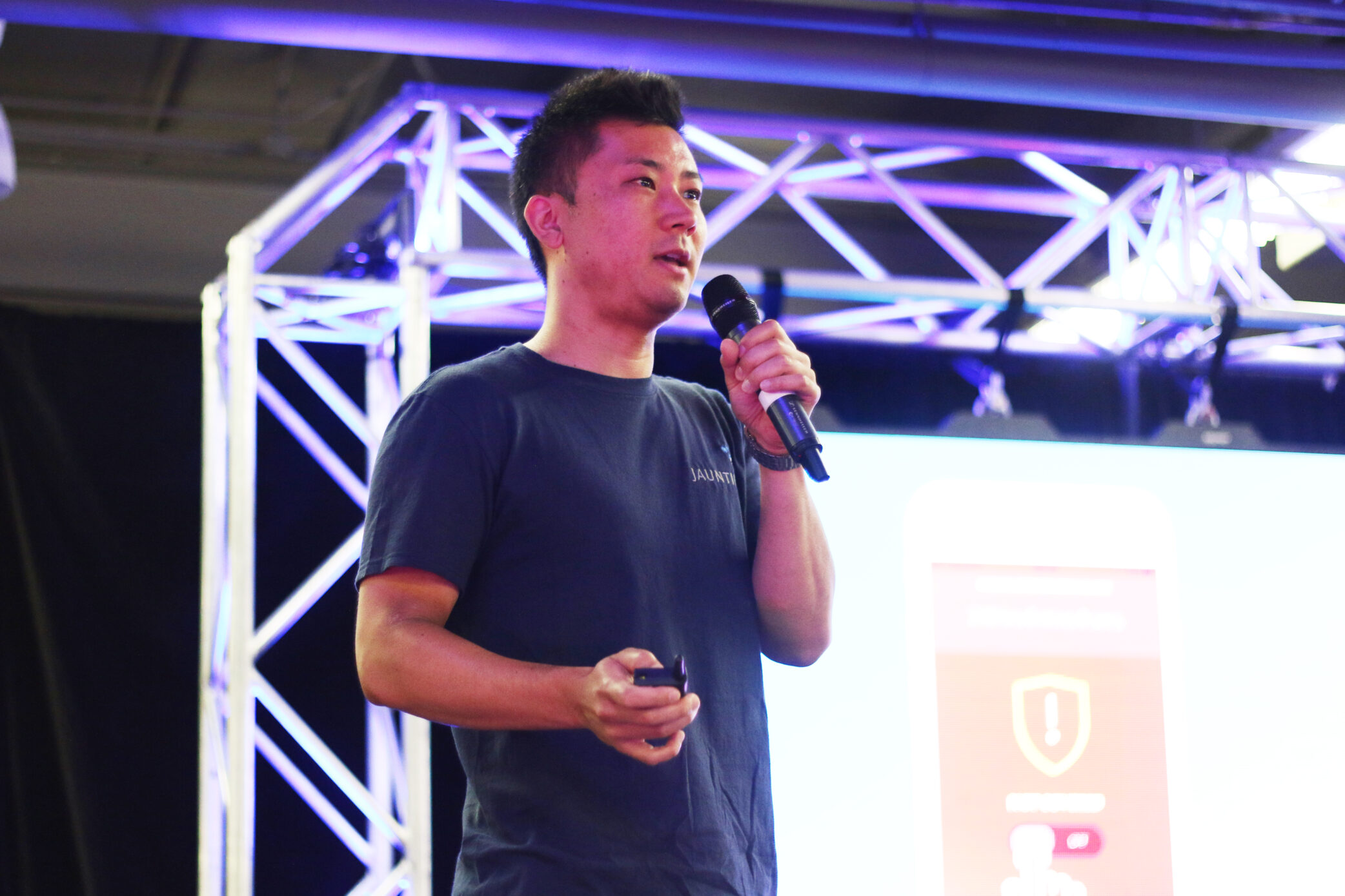 Image of a man speaking into a microphone on stage, while giving a pitch presentation in the CNE Gaming Garage.