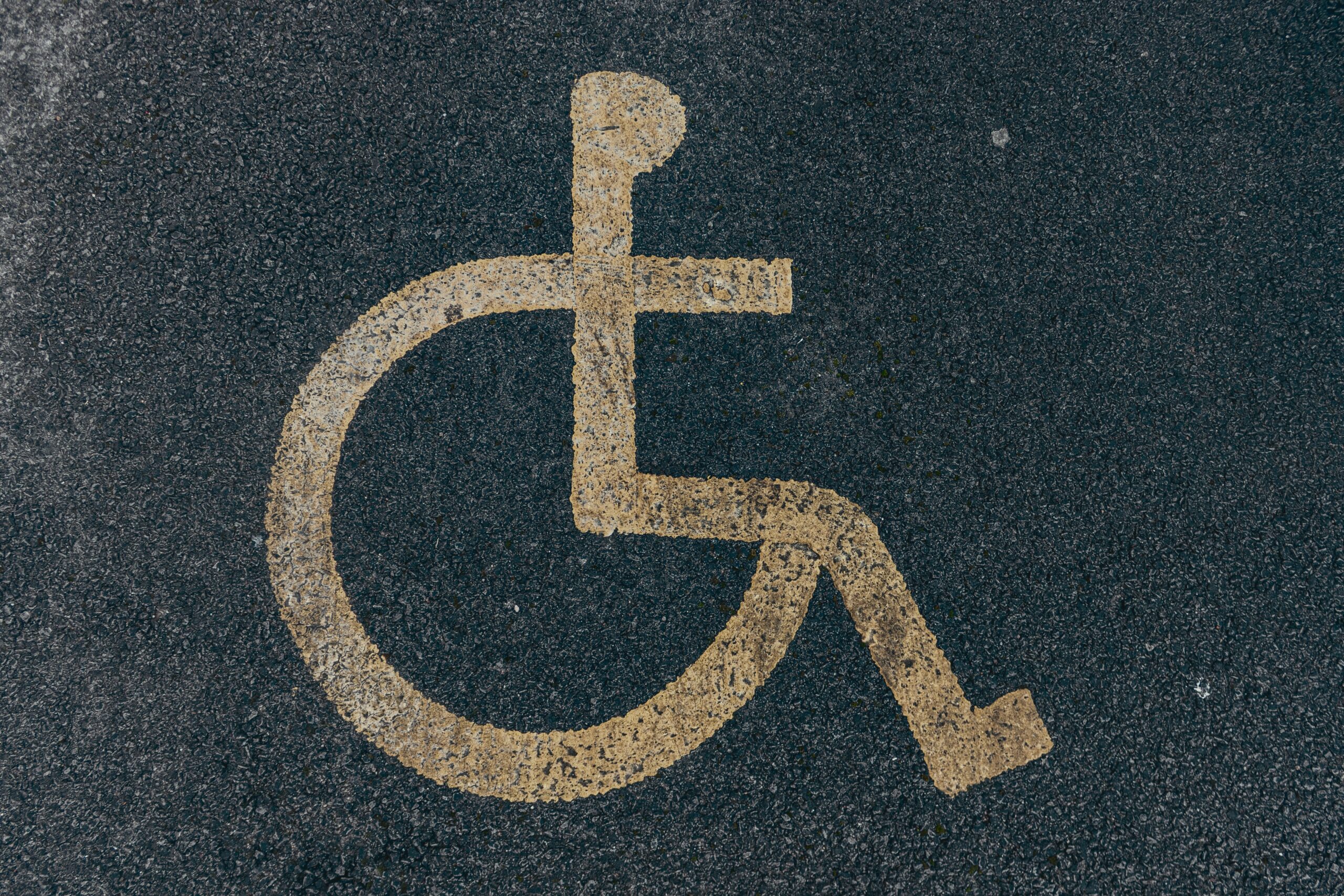Image of a wheelchair icon on painted in white on black pavement.