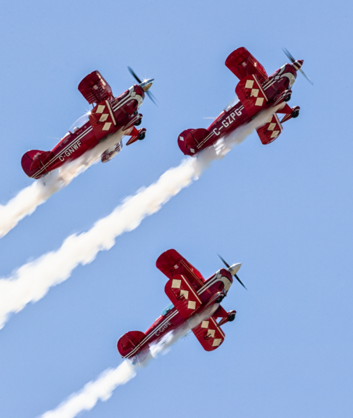 Air Show. Image of three red planes flying in formation in a blue sky.